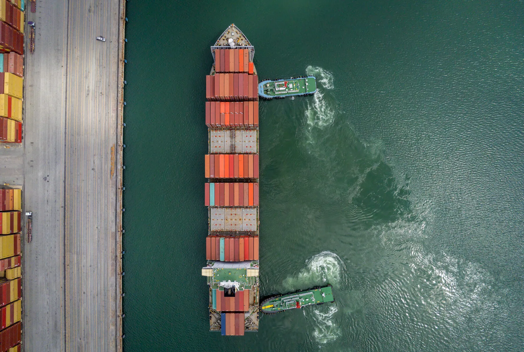 Vessel alongside a quay with two tugs, seen from above (illustrative)