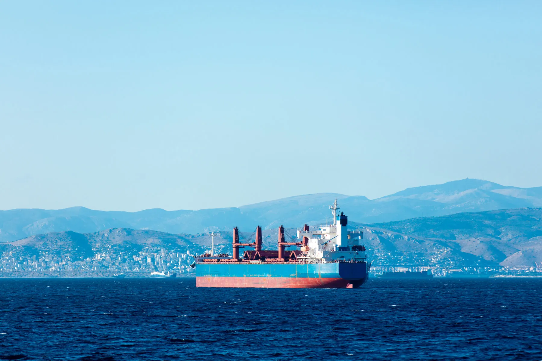 Bulk carrier under way on open water, mountains on the horizon (illustrative)